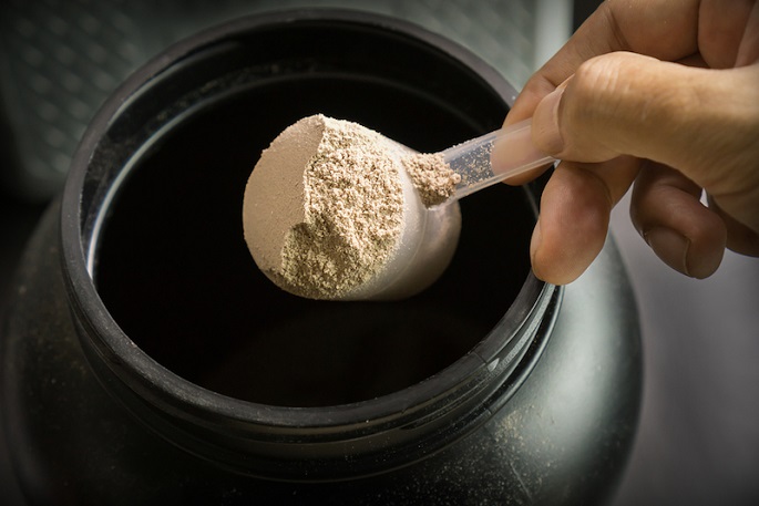 a person scooping protein powder from tube