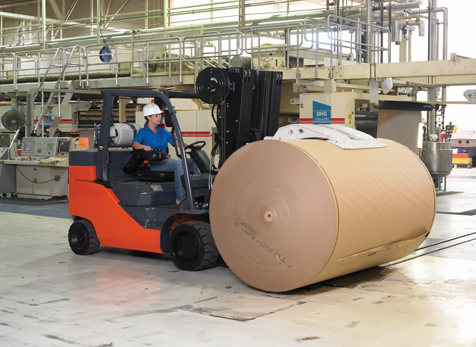 Woman driving forklift with paper clamp attachment with paper roll 